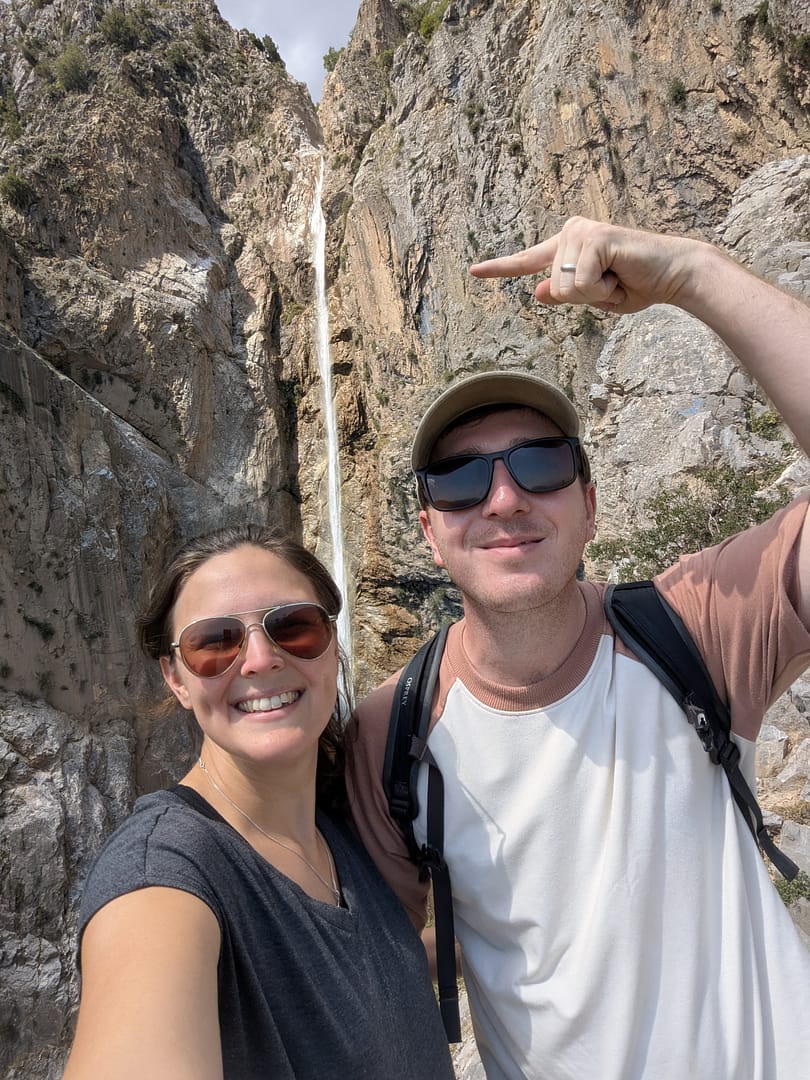 Sarah and Callum standing in front of a dramatic waterfall in Georgia, capturing the essence of their travel adventures and travel blog.
